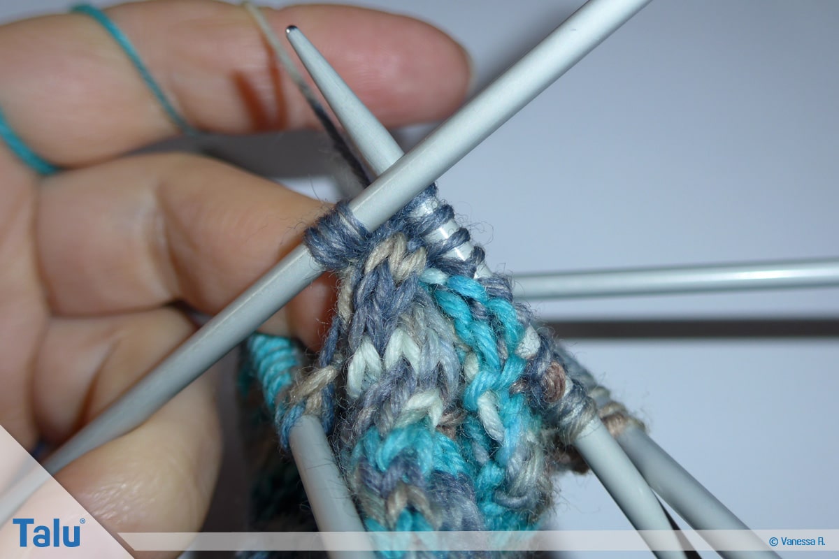 Socken mit Muster stricken, Zusatznadel hinter Strickarbeit legen